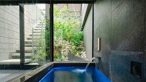 A modern spa with a hot tub, stone walls, and a view of a garden.