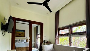 A modern living room with a sofa, a wooden bench, a ceiling fan, and a television mounted on the wall. - Mandala Homestay  (Ubud)