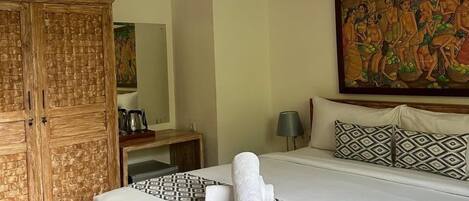 A hotel room with a large bed, a wooden wardrobe, a painting on the wall, and a bedside table with a lamp.