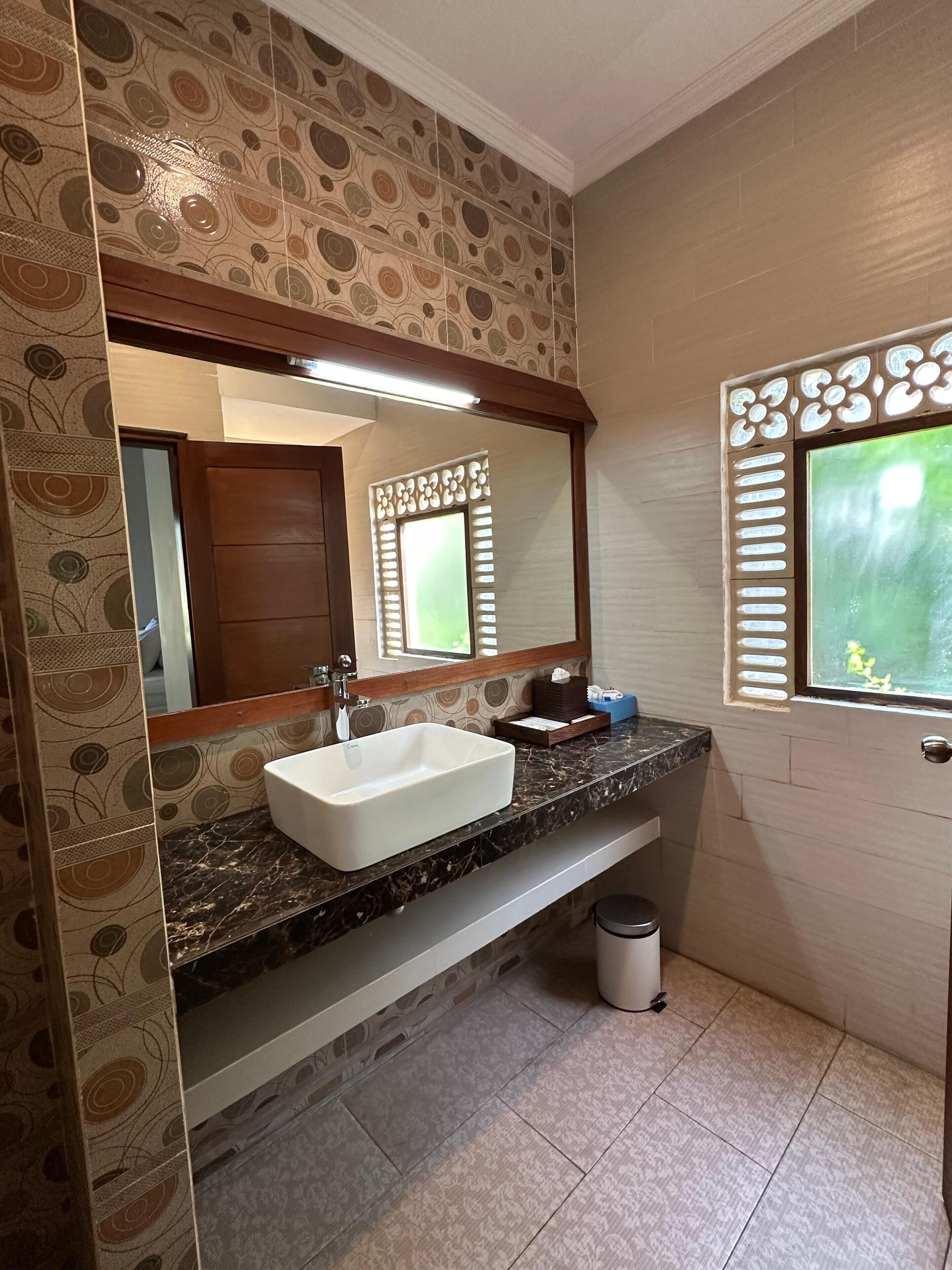 A bathroom with a white sink, a mirror, and patterned wallpaper.