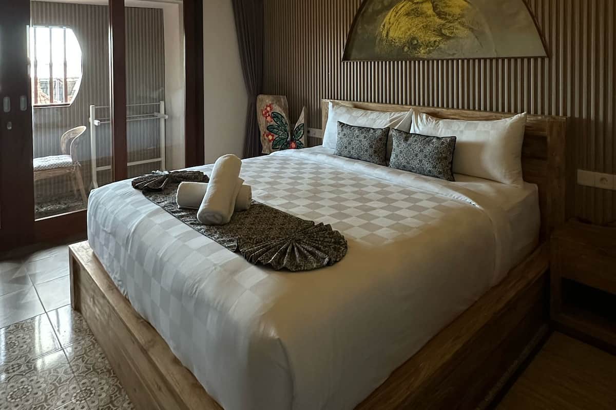 A large bed with a wooden headboard, a decorative wall panel, and a ceiling light fixture.
