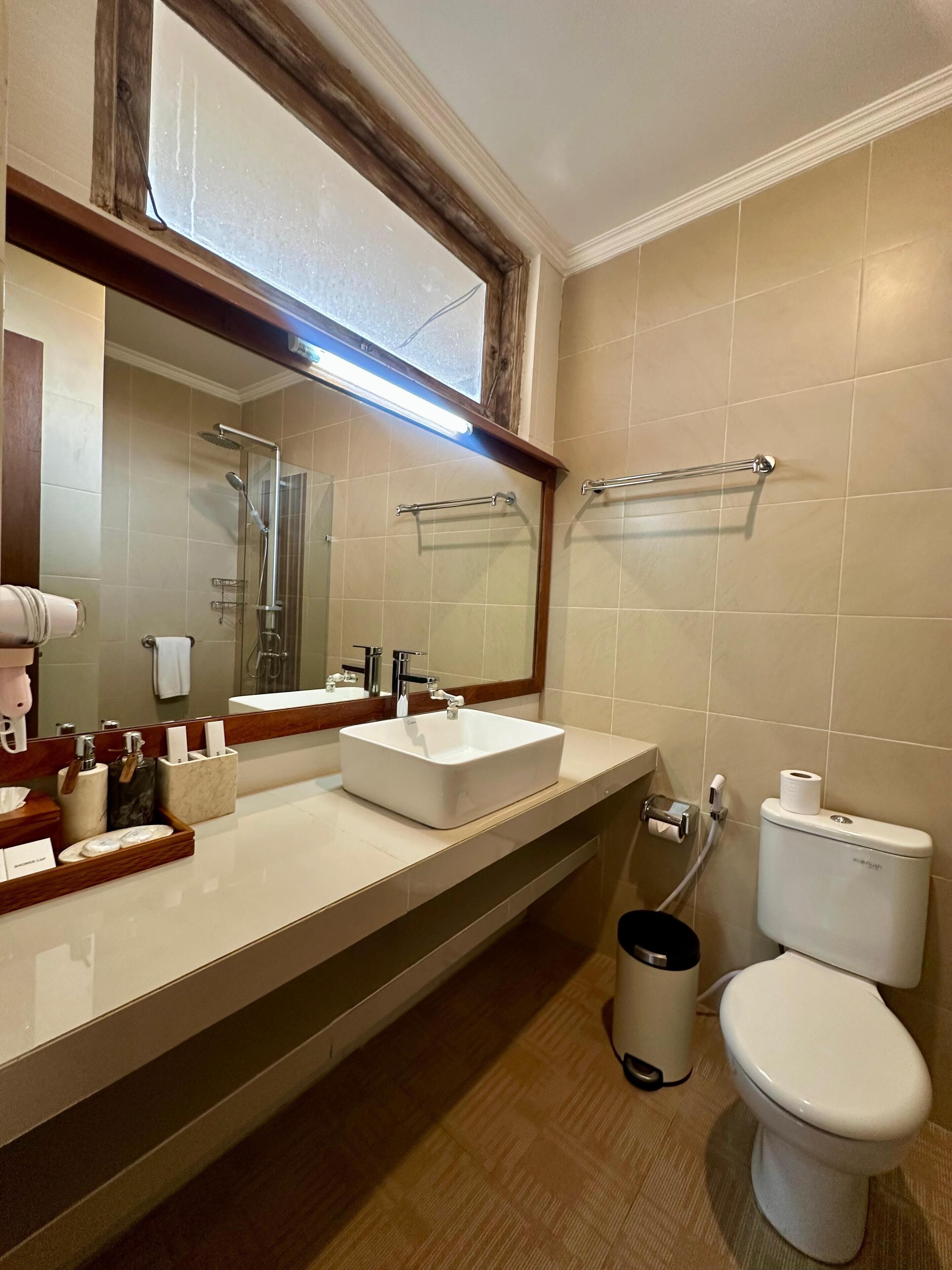 Un bagno con un grande specchio, due lavandini, un water e una doccia.