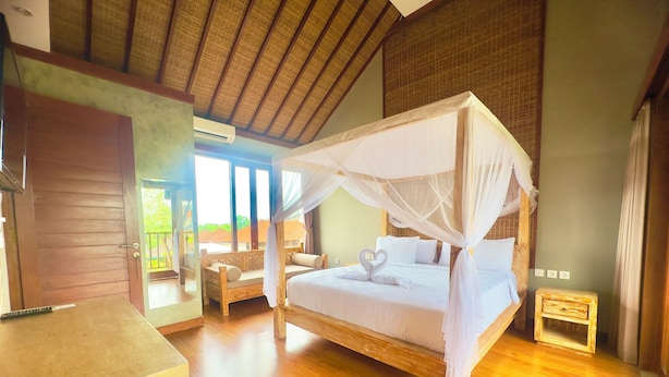A room with a wooden floor, a bed with a canopy, a bench, and a small table. - Mandala Homestay  (Ubud)