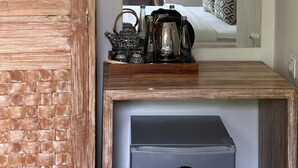 A room with a wooden cabinet, a small wooden table with a tray holding a teapot, cups, and a kettle. A mirror reflects a bed with pillows and a nightstand. - Mandala Homestay  (Ubud)