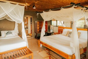 Una habitación con dos camas de madera, cada una con ropa blanca y dosel. Hay mesitas de noche de madera y una pequeña mesa.