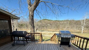 A wooden deck with two barbecue grills, a wooden fence, and a view of a hilly landscape. - The Hidden Cove on the Horseshoe (Canyon Lake)