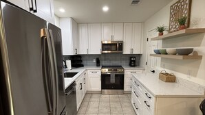 A modern kitchen with white cabinets, stainless steel appliances, and a tiled floor. - The Hidden Cove on the Horseshoe (Canyon Lake)