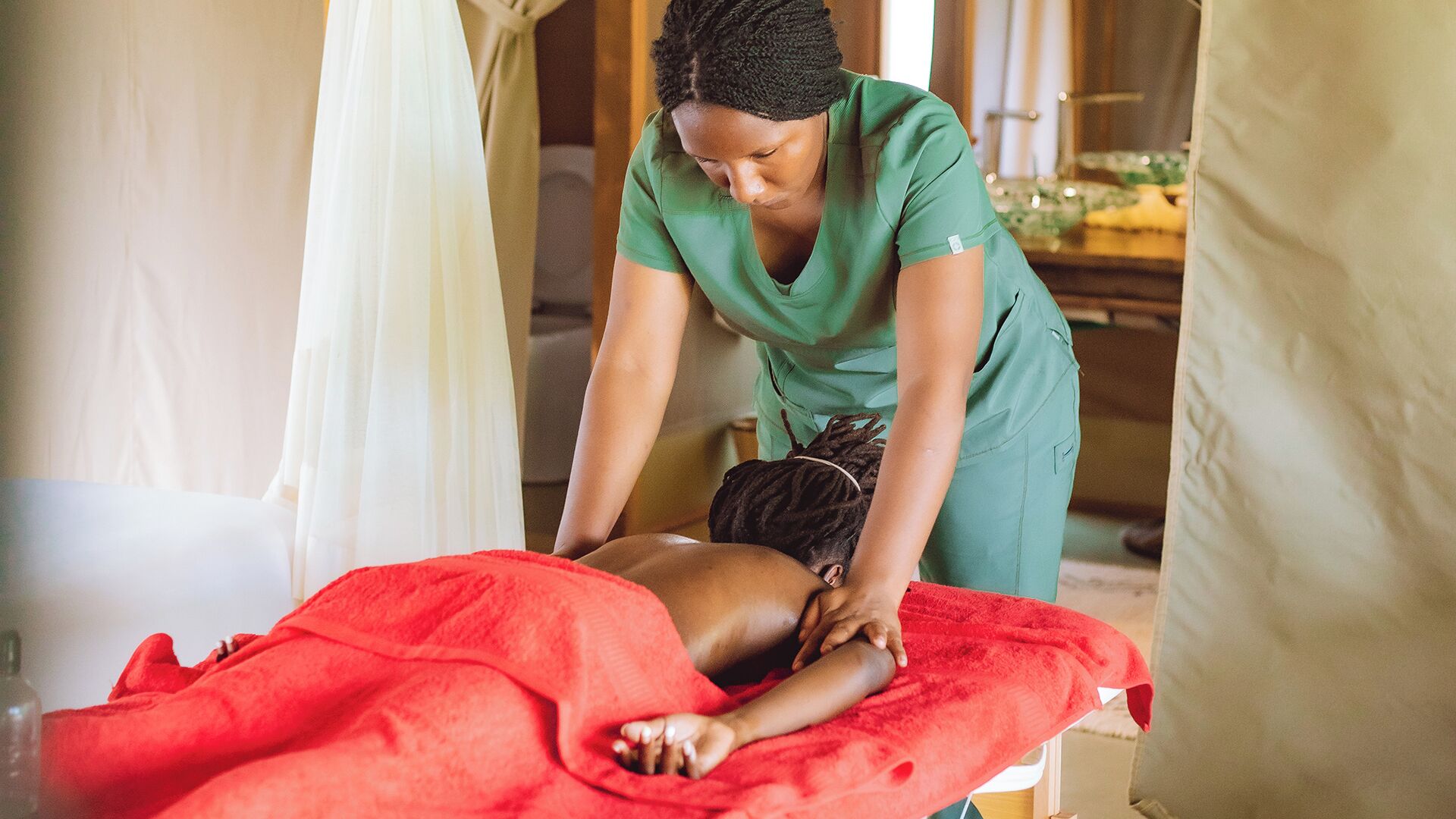 Eine Person erhält eine Massage in einem Raum mit einem roten Handtuch und einem weißen Vorhang.