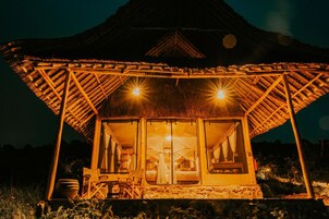Una estructura con techo de paja, con una cama y una mesita, iluminada por luces cálidas.