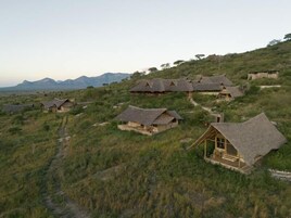 Una serie de casas de campo con techos de paja en una ladera cubierta de hierba, con una montaña al fondo.