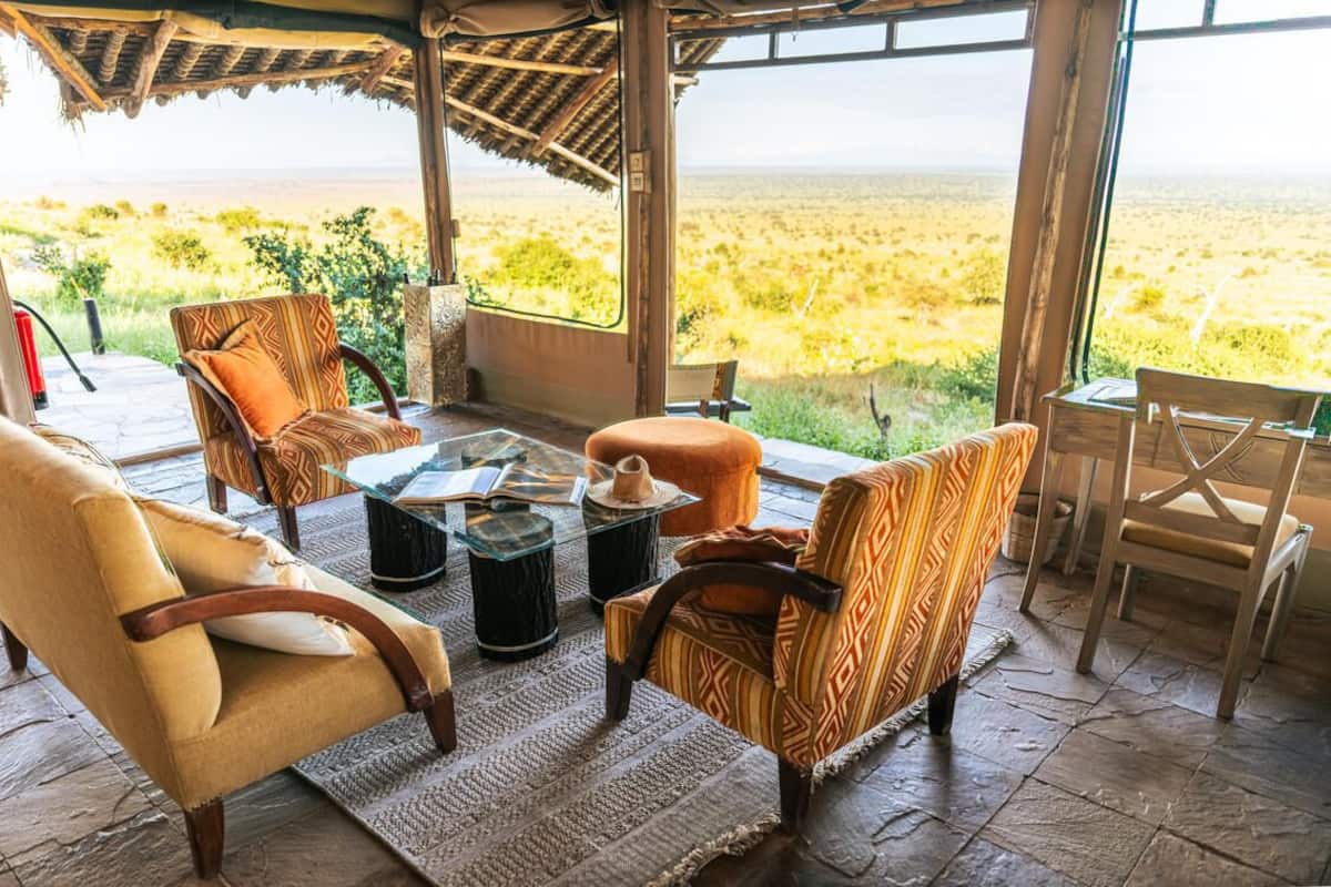 Uma área de estar aconchegante ao ar livre, com cadeiras de vime e uma mesa com tampo de vidro, com vista para uma paisagem extensa.