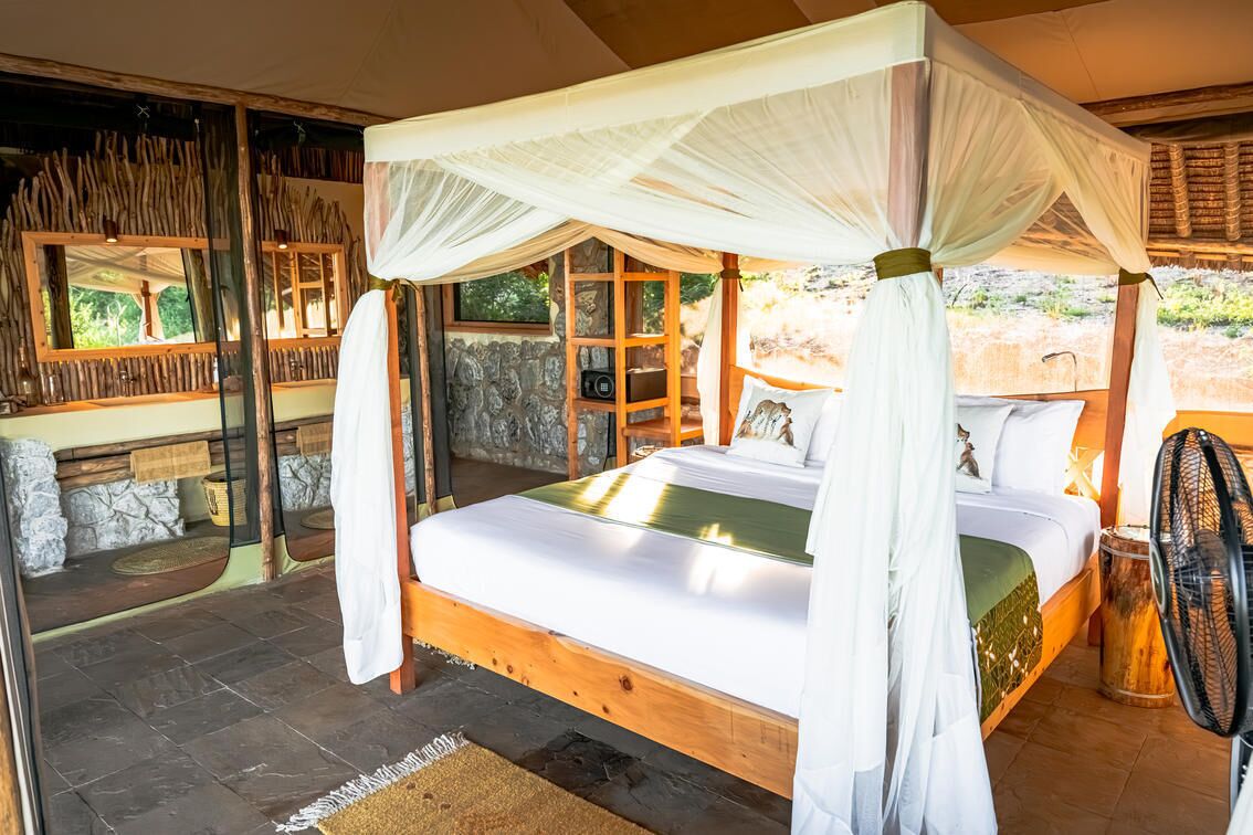 A room with a four-poster bed, stone walls, and a large window.