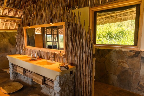 A bathroom with a stone sink, wooden wall decor, and a window with a view of greenery. - Soroi Cheetah Tented Camp (Maktau)