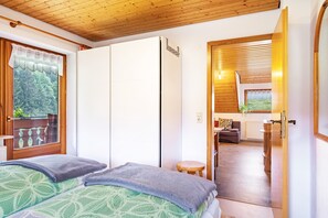 A bedroom with a bed, a wooden ceiling, a window with curtains, and a view of a living area.