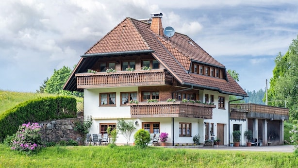 Ein zweigeschossiges Haus mit einem geneigten Dach, Holzbalkonen und einer Steinmauer.