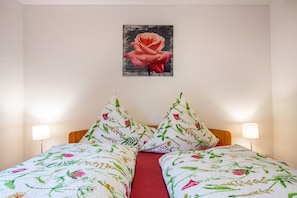 Un lit double avec une literie à motifs floraux, un seul tableau représentant une rose accroché au mur et des lampes de chevet.