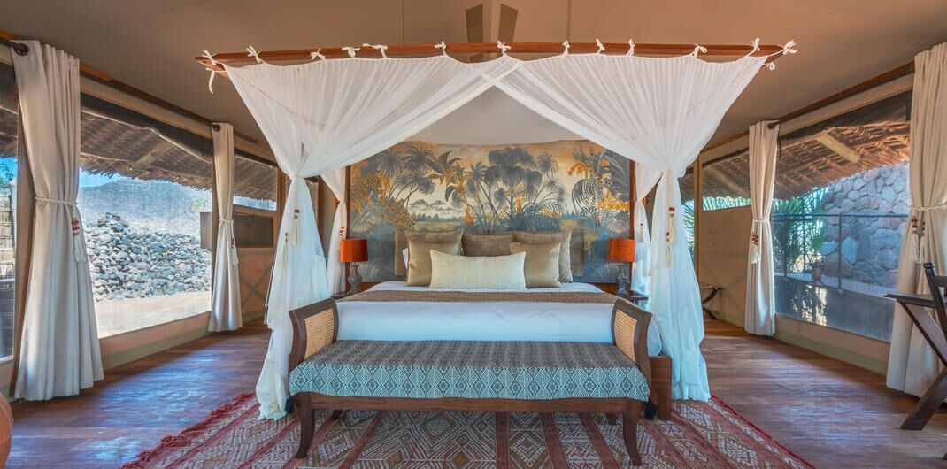 A large bed with a canopy, a mural on the wall, and a view of the outdoors.