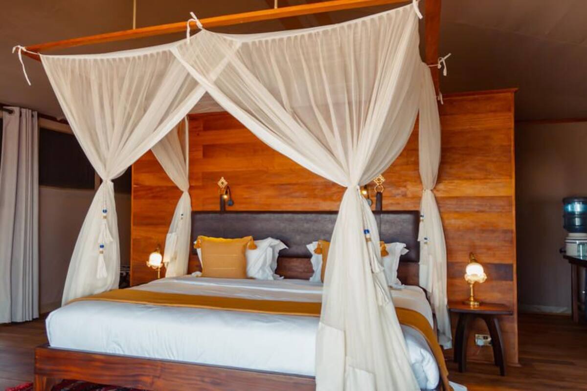 A large bed with a canopy, wooden headboard, and bedside lamps.