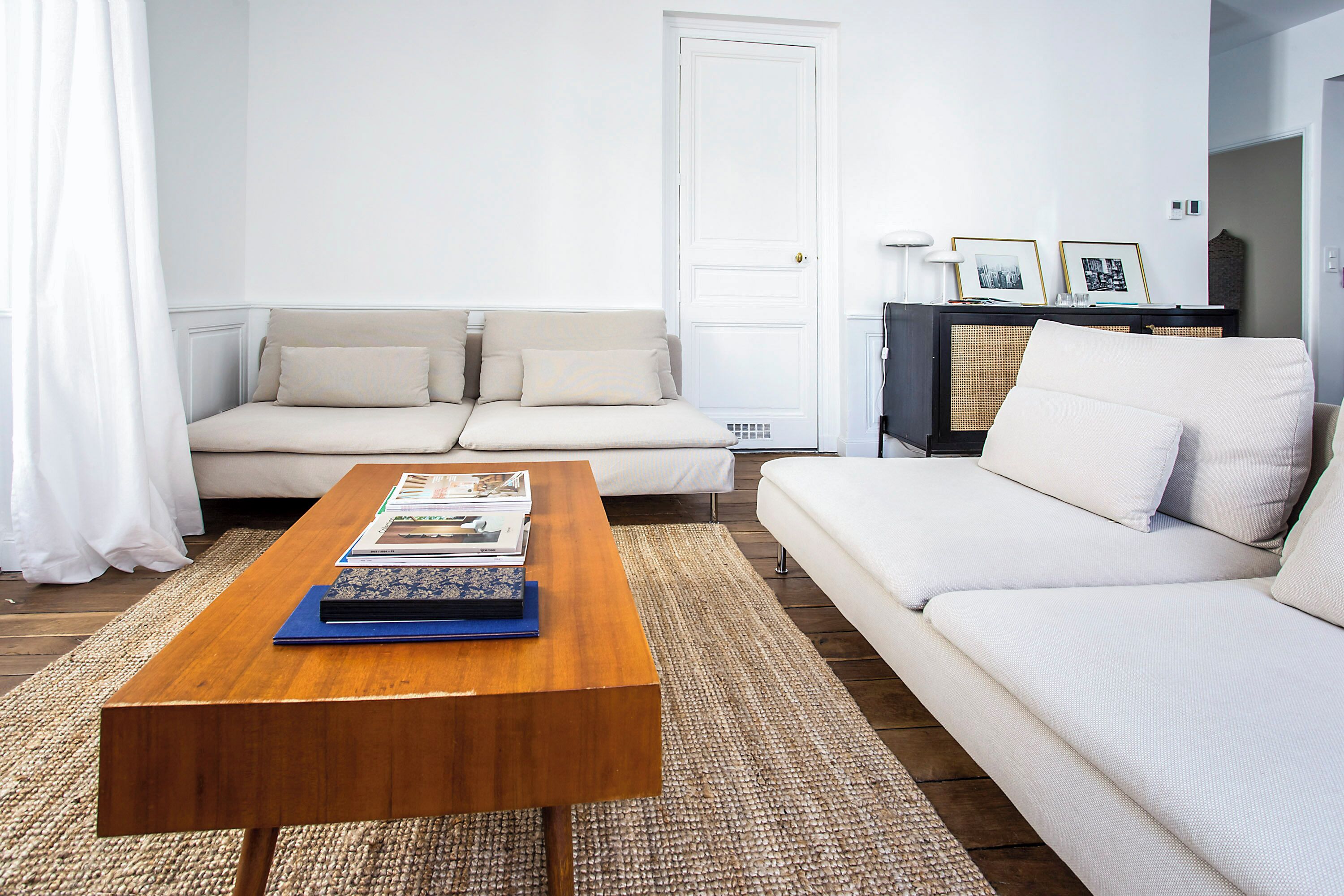 A living room with a wooden coffee table, two white sofas, and a black entertainment unit with framed pictures.