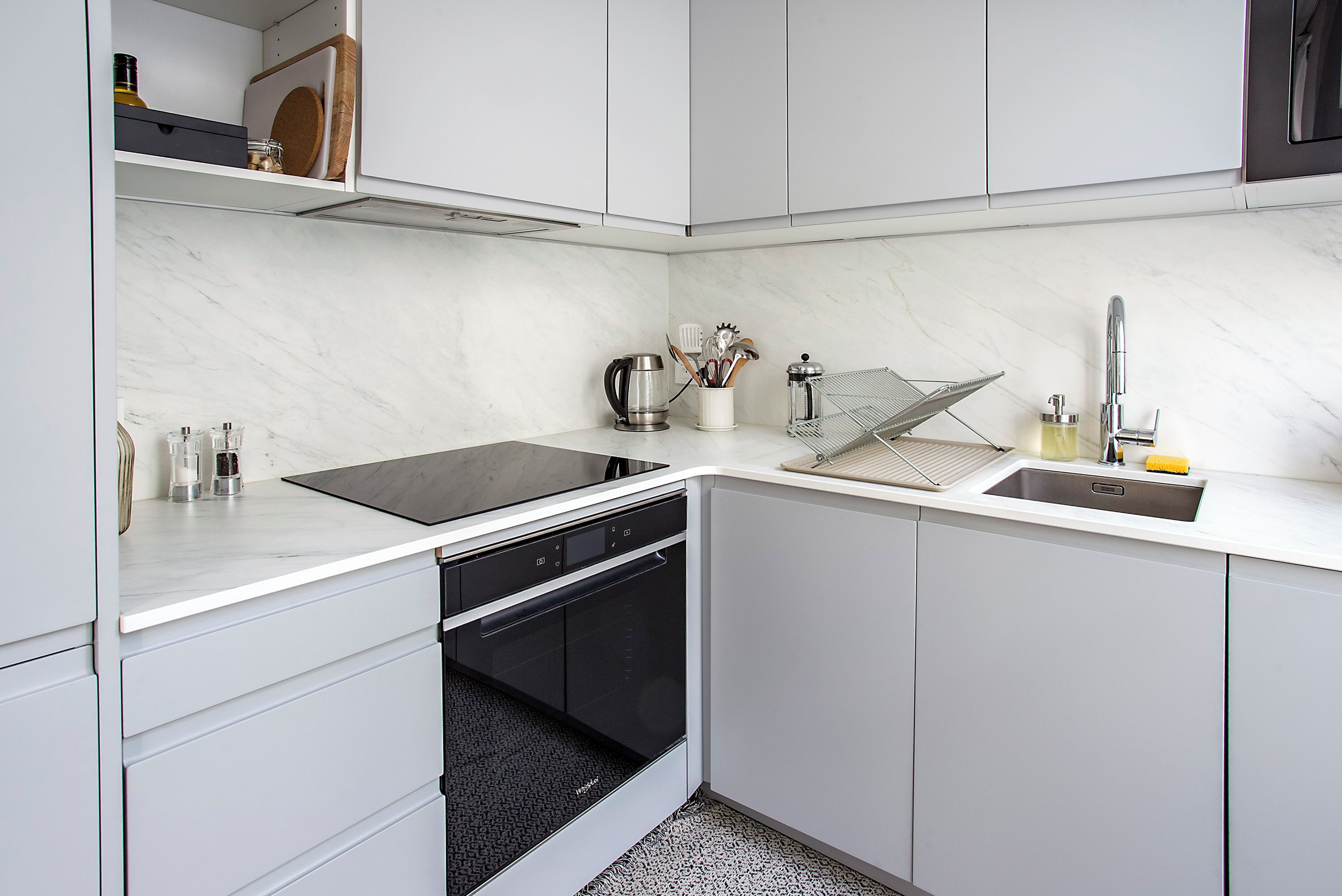 Une cuisine compacte avec des meubles blancs, un lave-vaisselle encastré, un évier avec un robinet et un plan de travail sur lequel sont disposés divers ustensiles de cuisine.