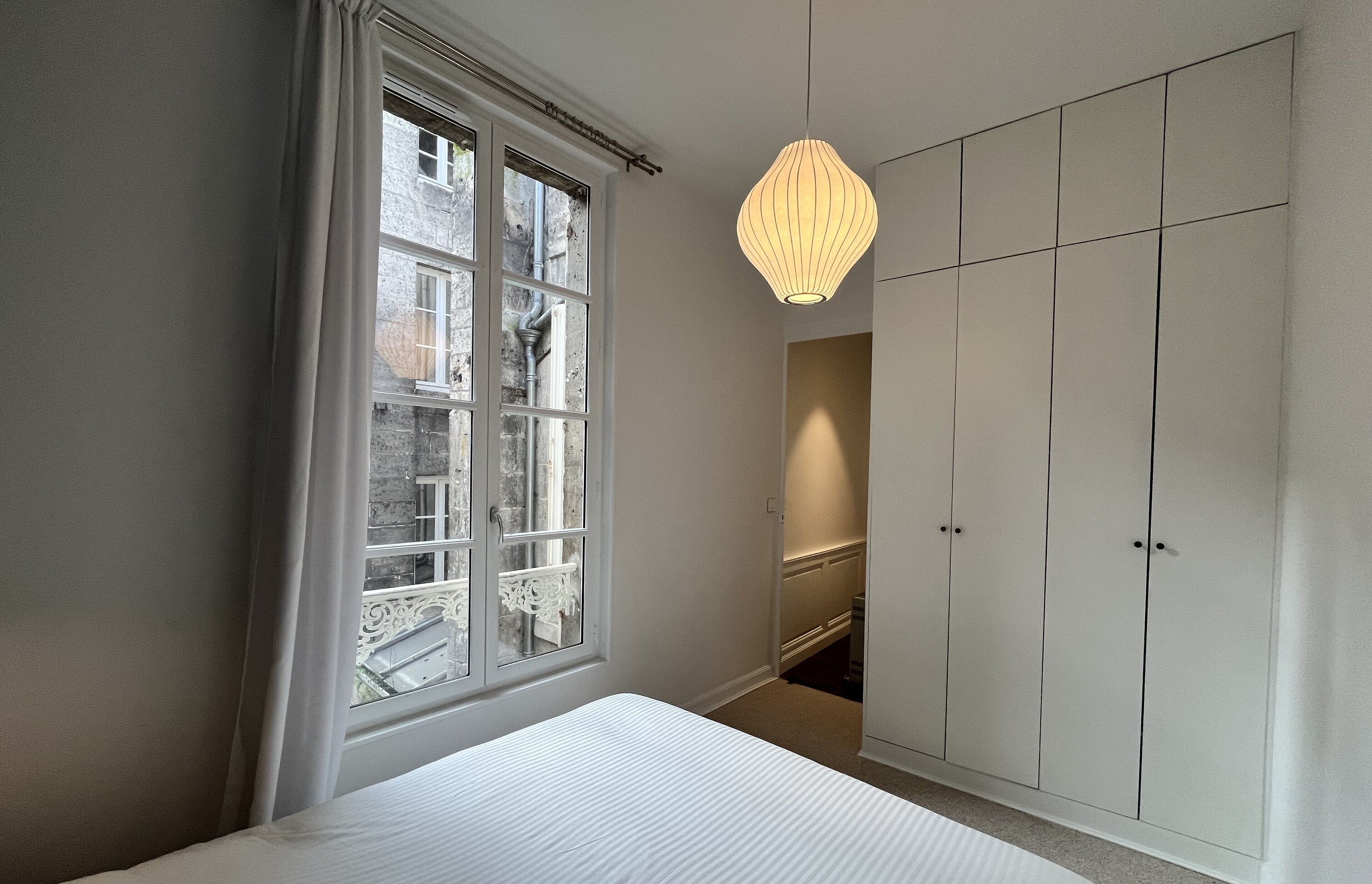 A bedroom with a large window, a bed, and a wardrobe.