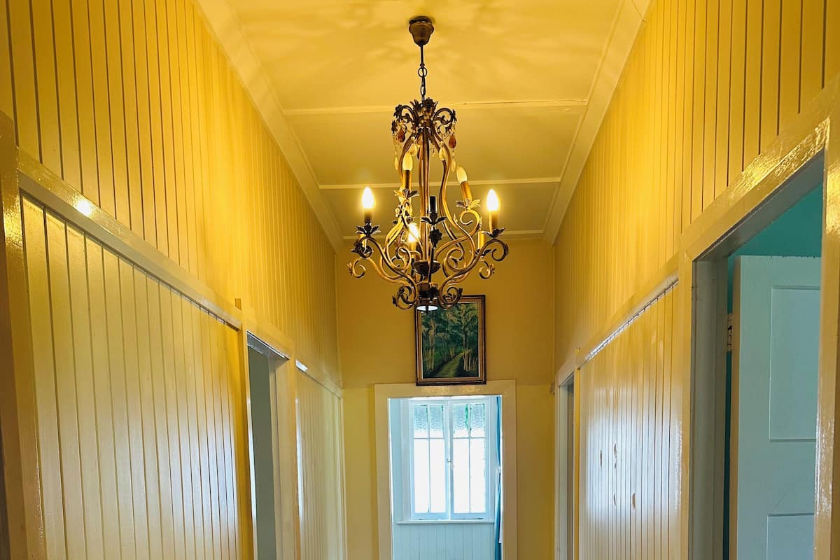 A hallway with wooden floors, white walls, and a chandelier. There is a bench along the left wall and a door on the right.