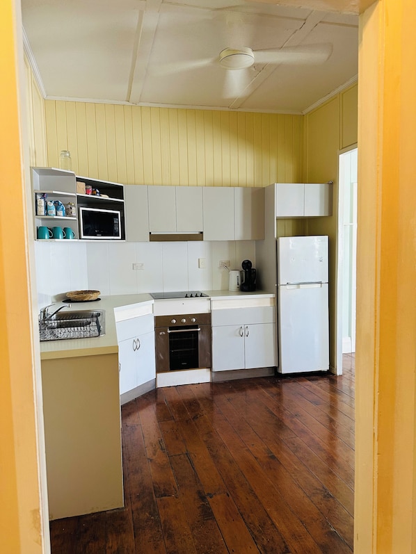 A compact kitchen with white cabinets, a microwave, a stove, and a refrigerator. - Mossman Exchange & Backpacker Resort (Mossman)