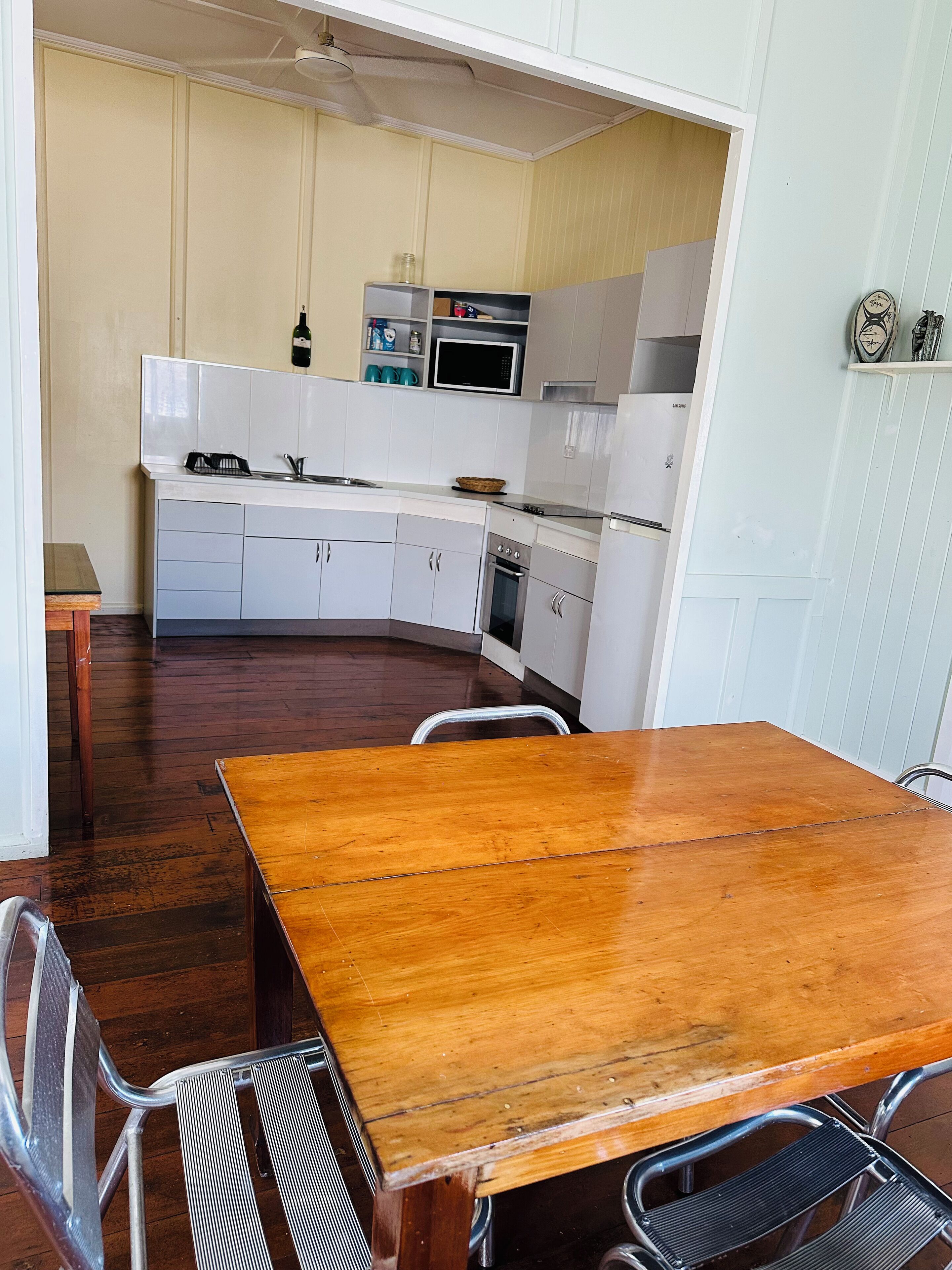 A compact kitchen with white cabinets, a microwave, and a stove. There's a wooden table with metal chairs in the foreground.