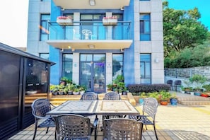 An outdoor seating area with a table and chairs, a building with a balcony, and potted plants.
