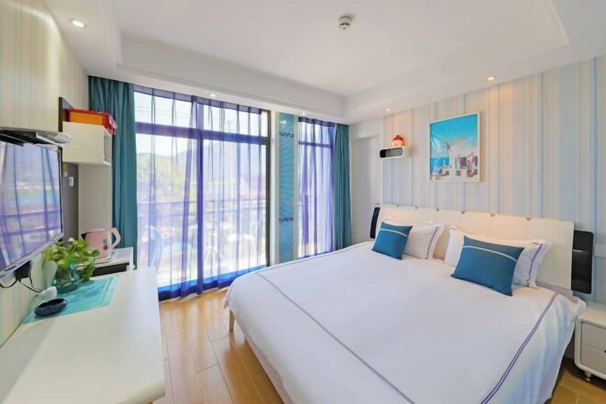 A hotel room with a large bed, a desk with a computer, a window with curtains, and a painting on the wall.