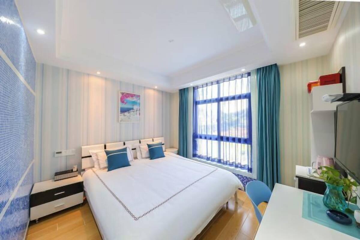 A hotel room with a large bed, a desk, a chair, a TV, and a window with curtains.