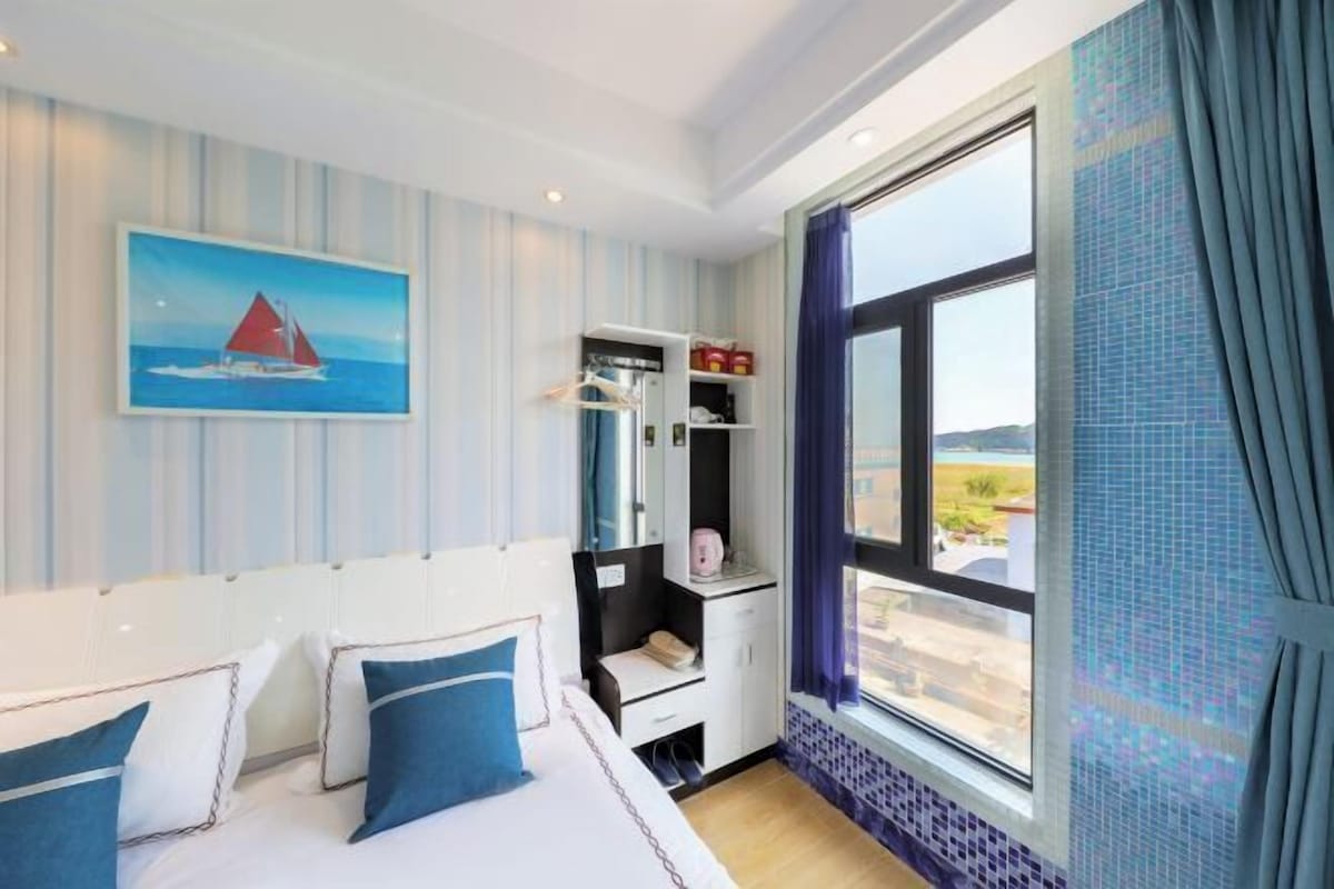 A hotel room with a bed, a wardrobe, a small desk, and a large window with a view of the landscape.