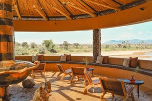 Un espacio al aire libre con sillas de madera y techo de paja, con vistas a un paisaje desértico.