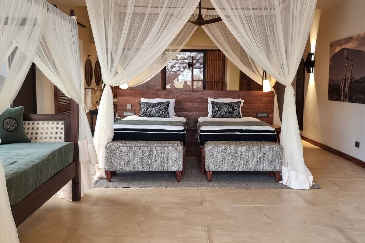 A room with two beds, each with a canopy, a bench, and a view of a mountain.