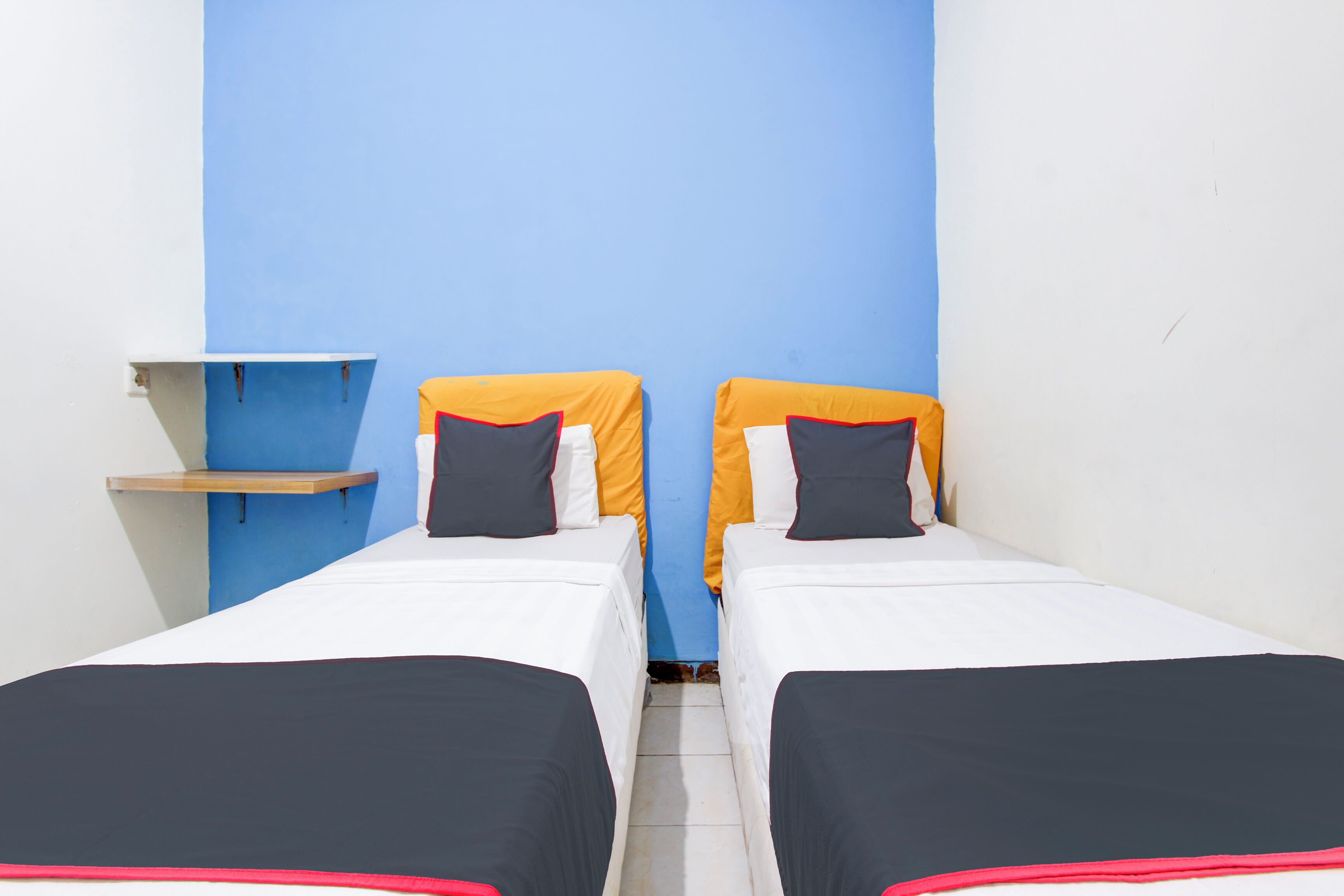 A room with two single beds, a small wooden shelf, and a blue wall.