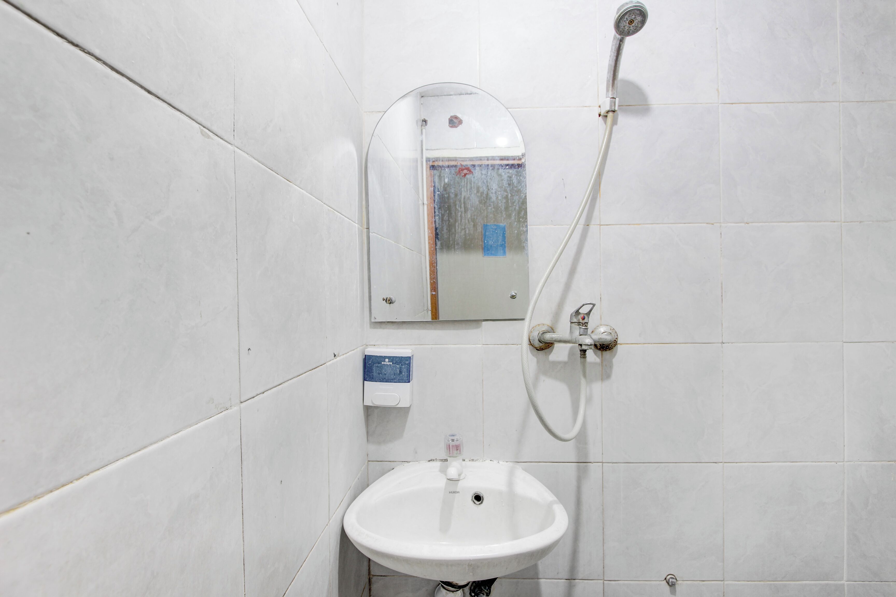 A bathroom with white tiles, a white sink, a mirror, and a shower.