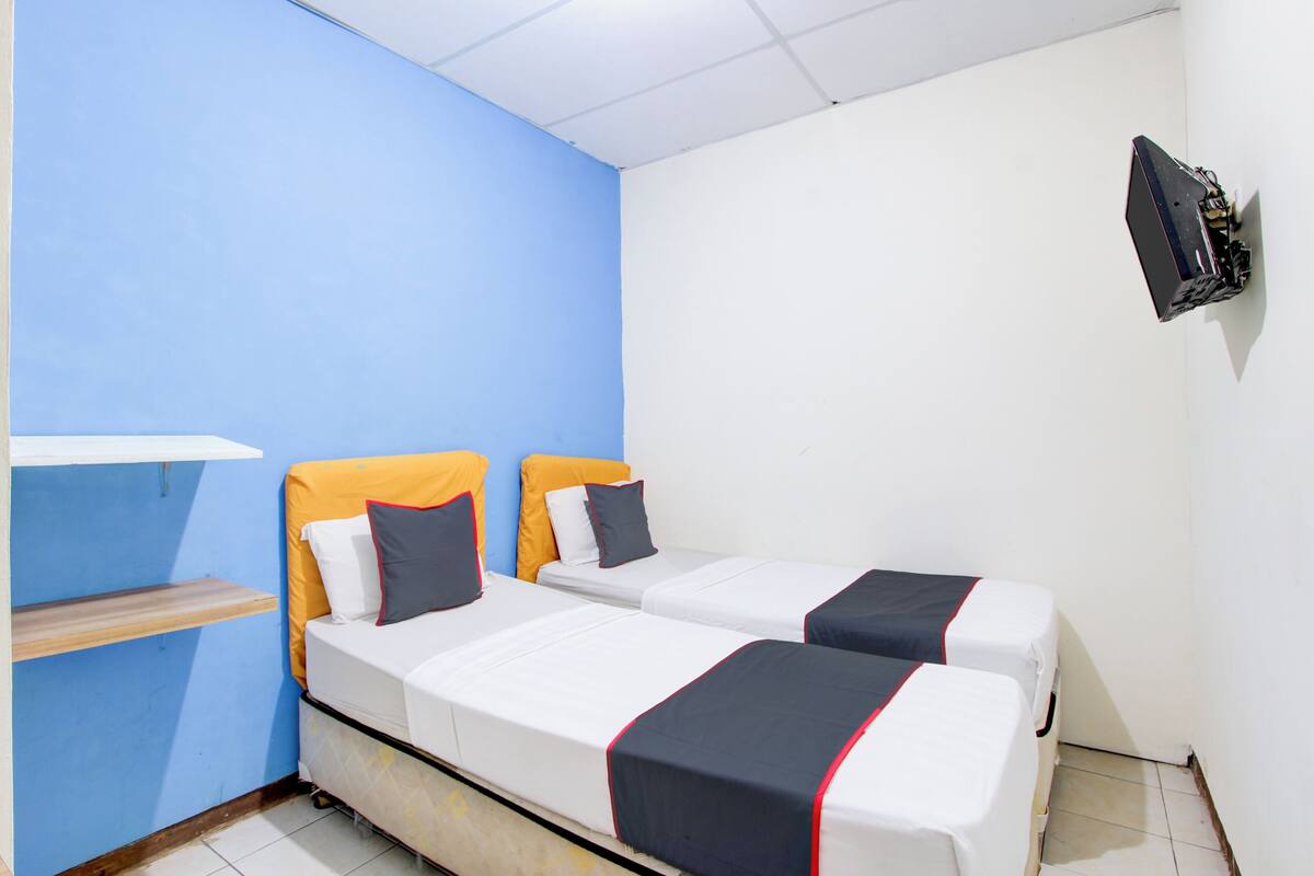 A room with two beds, a shelf, and a TV mounted on the wall.