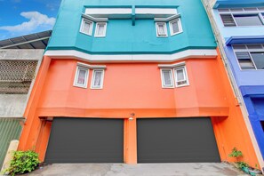 A two-story building with a teal upper floor and an orange lower floor, featuring two garage doors and small windows.