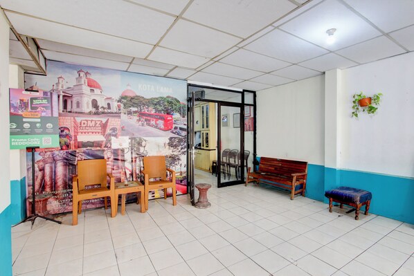 A room with a tiled floor, wooden chairs, a bench, a small table, and a wall with a poster.