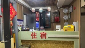Zona de recepción de hotel con mostrador verde, un pequeño espacio de asientos y relojes en la pared.