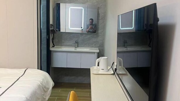 Habitación de hotel con cama, escritorio, silla, espejo, lavamanos y cafetera.