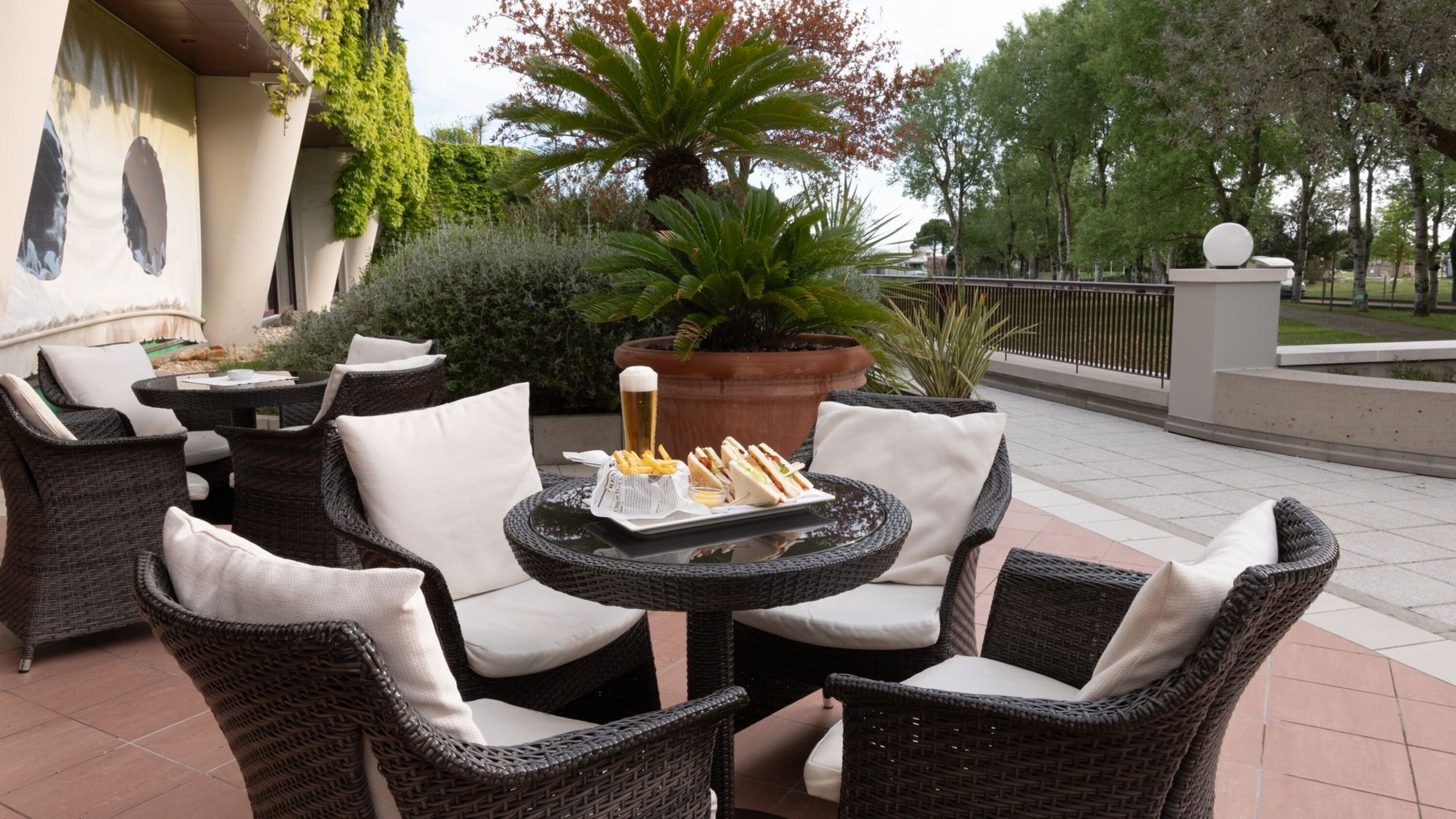 Un espace extérieur aménagé avec des chaises en osier et une table, un pot de fleurs et une bouteille de bière.