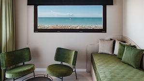 A room with a large window overlooking a beach, a green sofa, and two green chairs.