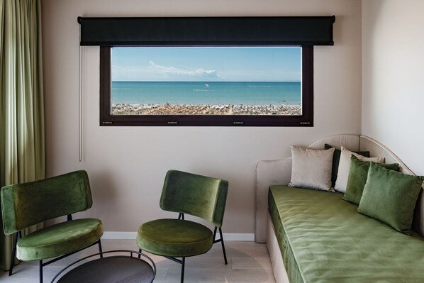 Una habitación con un amplio ventanal con vistas a una playa, un sofá verde y dos sillas verdes.