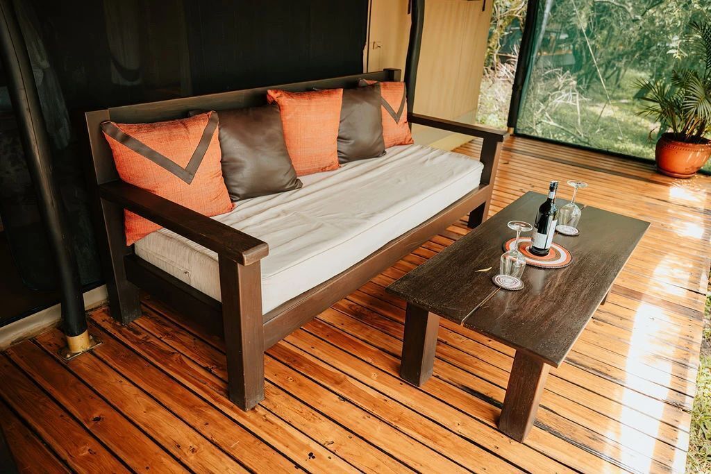 A wooden floor, a sofa with cushions, and a table with glasses and bottles.