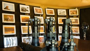 A room with a wooden table displaying multiple cameras and lenses. - Soroi Private Camp (Maasai Mara)