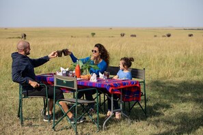 Eine Familie speist an einem Tisch im Freien in einer grünen Wiese mit freiem Blick auf die Landschaft.