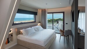 Habitación de hotel moderna con una cama grande, un escritorio y un balcón con vistas a la playa.