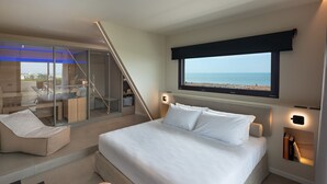 Un dormitorio moderno con una cama grande, un balcón con paredes de vidrio y vistas a la playa.