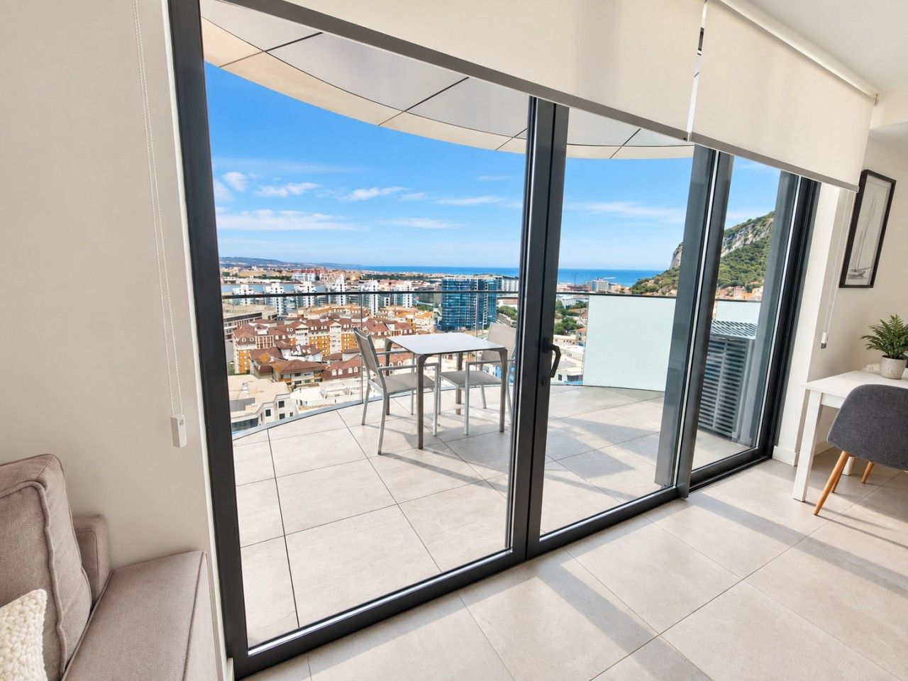 Un apartamento moderno con un gran ventanal corredero que da a un balcón con vistas a la ciudad.